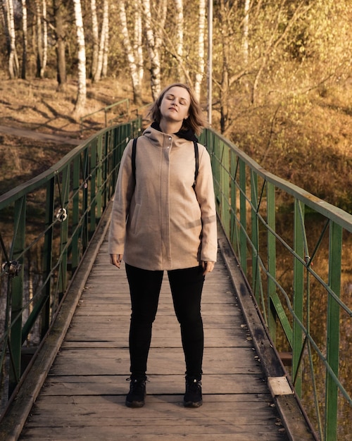 Portret van een aantrekkelijke vrouw die op de brug over de rivier staat in het herfstpark authentieke mensen