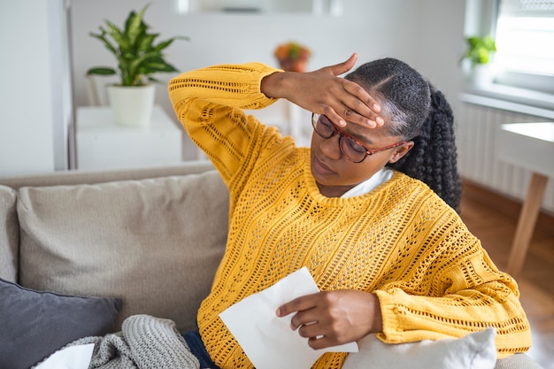 Portret van een aantrekkelijke vrouw die thuis op een bank zit met hoofdpijn, pijn voelt en zich onwel voelt. Verstoorde depressieve vrouw die op de bank ligt en sterke hoofdpijn migraine voelt.