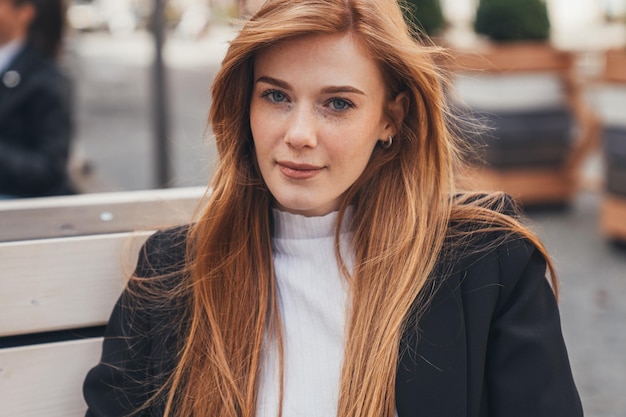 Foto portret van een aantrekkelijke vrouw met rood haar, zittend op een houten bankje in het park mooi jong meisje doordachte blik schoonheidsportret