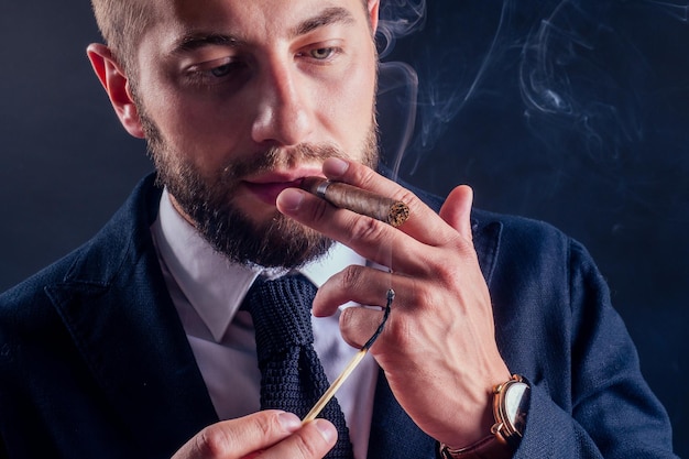 Portret van een aantrekkelijke zakenman met een sigaar in zwarte achtergrondstudio