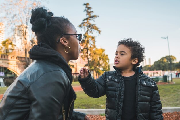 Portret van een Afrikaanse Amerikaanse moeder met zijn zoon die zich buiten in het park bevindt, die pret heeft