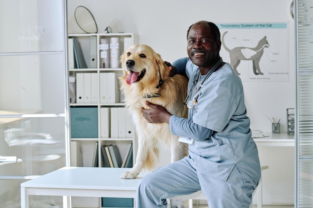 Portret van een Afrikaanse dierenarts-arts met een huishond die naar de camera glimlacht terwijl hij in de kliniek werkt