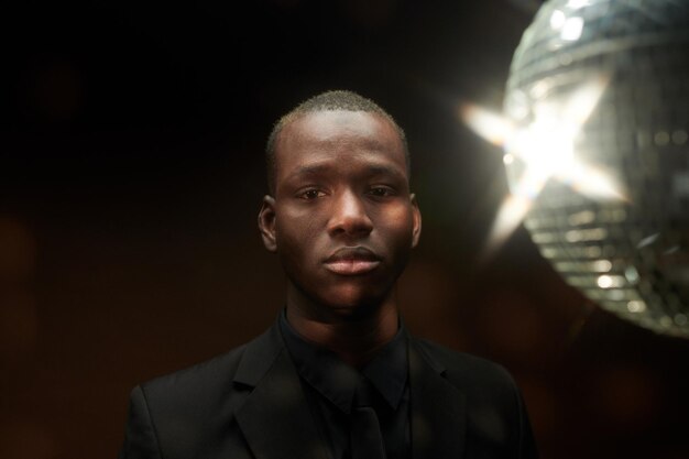 Portret van een Afrikaanse jongeman die naar de camera kijkt terwijl hij in het donker staat met een discobal bovenaan