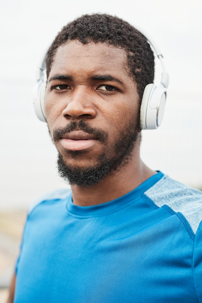 Portret van een Afrikaanse jongeman in een draadloze koptelefoon die naar de camera kijkt terwijl hij naar muziek luistert