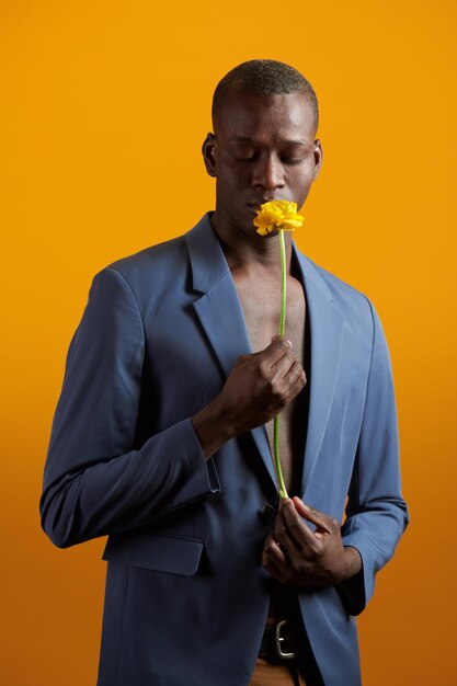 Portret van een Afrikaanse knappe man in pak die de bloem in zijn hand ruikt tegen de gele achtergrond