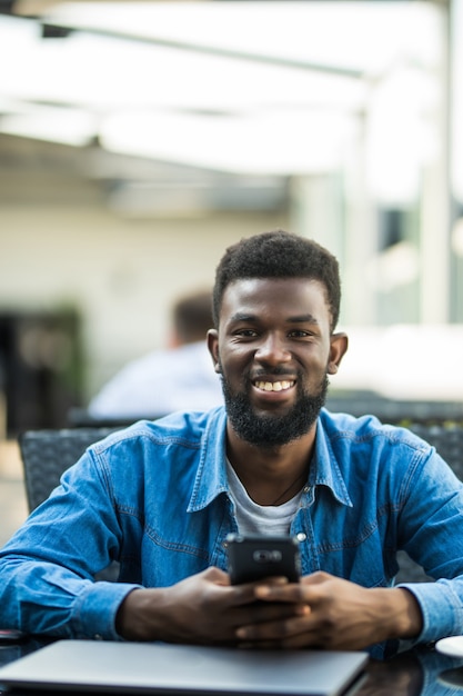 Foto portret van een afrikaanse man praten over de telefoon met laptop voor hem op tafel