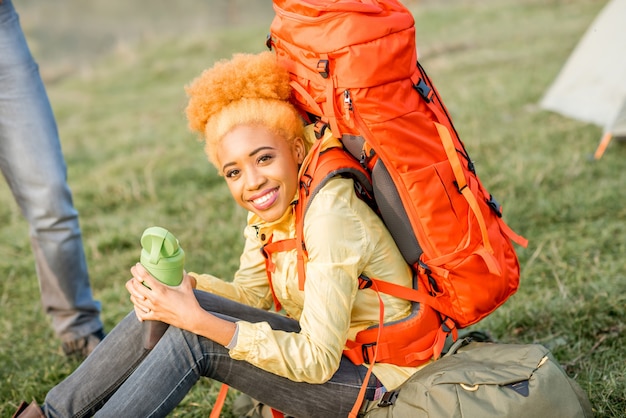 Portret van een Afrikaanse vrouw die met rugzak en fles buiten op het groene gazon rust