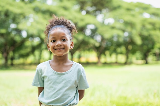 Portret van een Afro-Amerikaans meisje met krullend haar dat lacht en naar de camera in het park kijkt