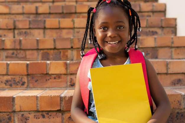 Portret van een Afro-Amerikaans schoolmeisje dat op de trap zit en boeken vasthoudt op de basisschool