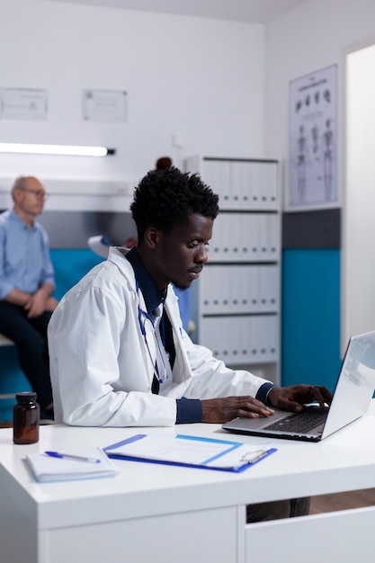 Portret van een afro-amerikaanse arts die aan een bureau zit met een laptop