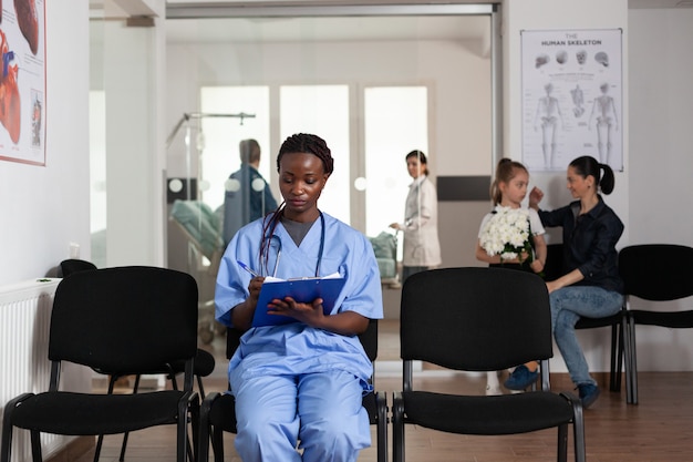 Portret van een Afro-Amerikaanse assistent die in de camera kijkt tijdens het schrijven van een hulpdienst voor de gezondheidszorg