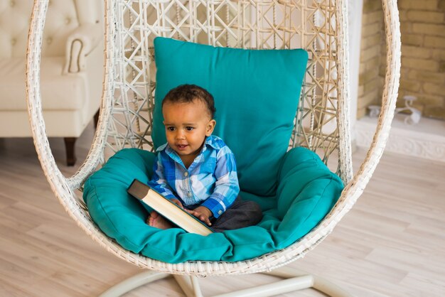Portret van een Afro-Amerikaanse babyjongen die een boek op de bank vasthoudt.
