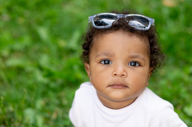 Portret van een Afro-Amerikaanse babyjongen op een groen grasveld in de zomer met een zonnebril op