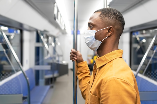 Portret van een Afro-Amerikaanse man met een beschermend masker die tijdens een pandemie in een metro rijdt