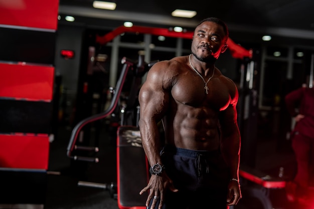 Portret van een Afro-Amerikaanse mannelijke fitnesstrainer Bodybuilder toont biceps en kijkt naar de achtergrond van de sportschool