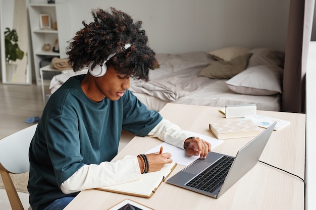 Portret van een afro-amerikaanse tiener die thuis of in een studentenkamer studeert en laptop kopieerruimte gebruikt