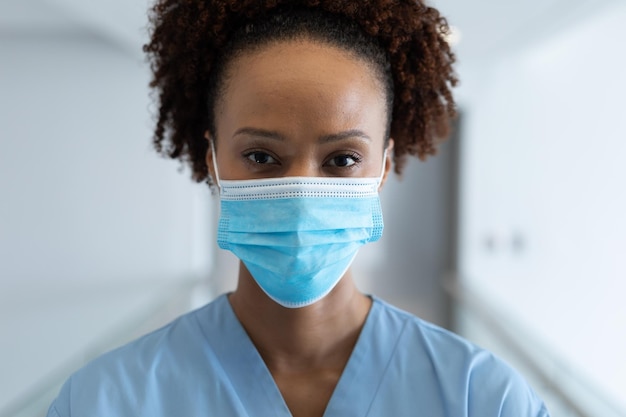 Portret van een Afro-Amerikaanse vrouwelijke arts met een masker in de ziekenhuisgang