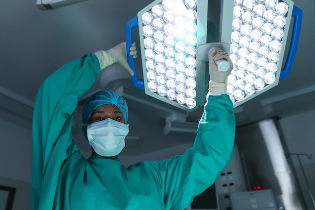 Portret van een Afro-Amerikaanse vrouwelijke chirurg die een chirurgisch gewaad en een gezichtsmasker draagt in de operatiekamer. Ziekenhuis, operatie, geneeskunde, gezondheidszorg en werk, onveranderd.