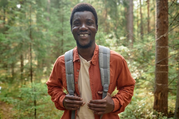 Portret van een Afro-Amerikaanse wandelaar met rugzak die glimlacht naar de camera terwijl hij in het bos reist