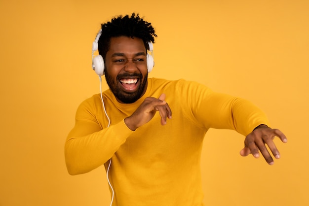 Portret van een afro-man die geniet van het luisteren naar muziek met een koptelefoon terwijl hij tegen een geïsoleerde gele achtergrond staat.