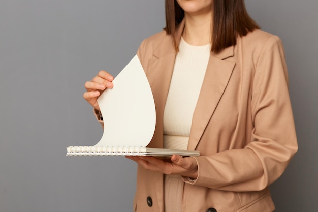 Portret van een anonieme anonieme vrouw, gekleed in een beige jasje in officiële stijl, geïsoleerd over een grijze achtergrond, papieren documenten omslaande pagina's aan het werk houdend