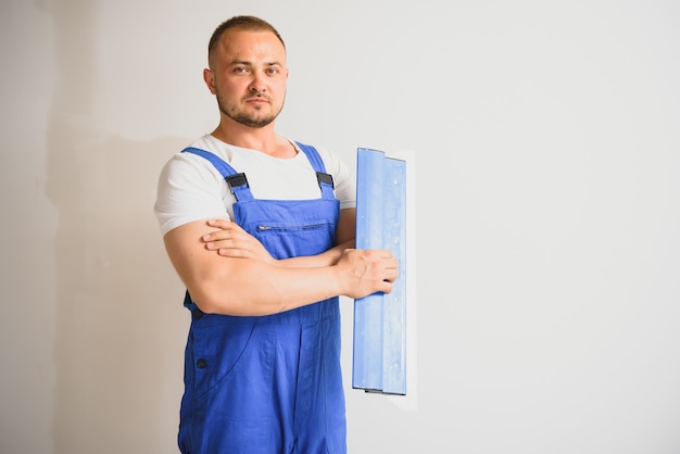 Portret van een arbeider in overall en met een plamuurmes in zijn handen tegen de gepleisterde muurachtergrond. Reparatiewerk en bouwconcept