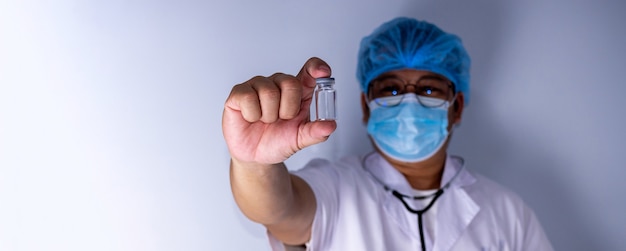 Portret van een arts die een masker draagt en een hoed draagt Staan met een lege vaccin- of pilfles. Medisch concept en behandeling.