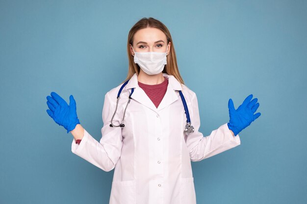 Portret van een arts in een witte jas, handschoenen en een medisch masker op een blauwe geïsoleerde achtergrond Influenza en SARS pandemie