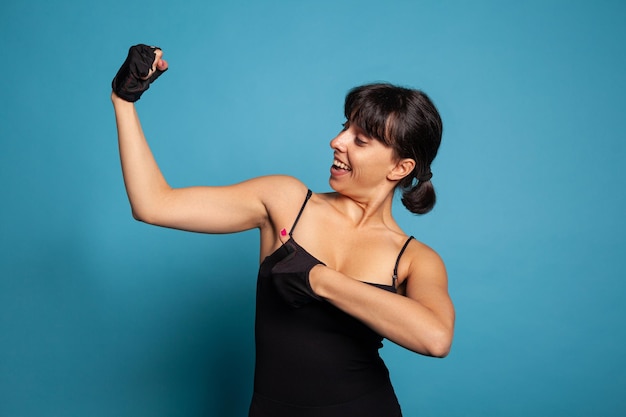 Portret van een atletische fitte vrouw in sportkleding die mijn spieren laat zien na het beëindigen van de fitnesstraining in de studio met blauwe achtergrond. Personal trainer werkt aan een gezonde levensstijl die sport beoefent