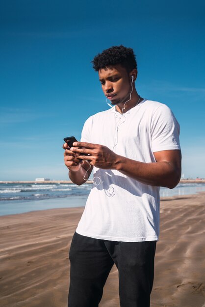 Portret van een atletische man die zijn mobiele telefoon gebruikt tijdens een pauze van de training op het strand.