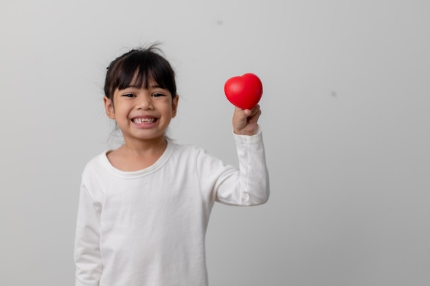 Portret van een Aziatisch klein meisje dat een rood hartteken op een witte achtergrond houdt