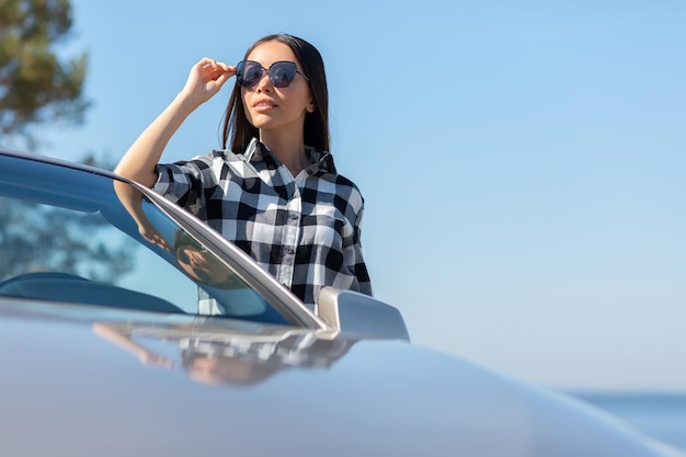 Portret van een Aziatisch meisje dat auto leunt en wegkijkt