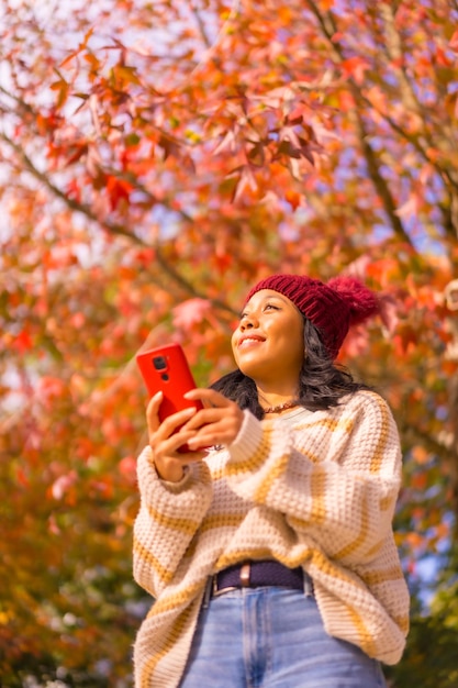 Portret van een aziatisch meisje in de herfst met een mobiel die glimlacht in een bos van rood bladerentechnologieconcept