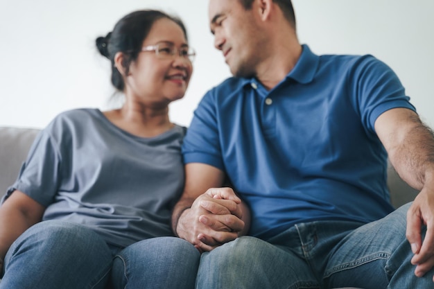 Portret van een Aziatisch volwassen stel dat in de woonkamer zit, vrouw en man knuffelen hand in hand