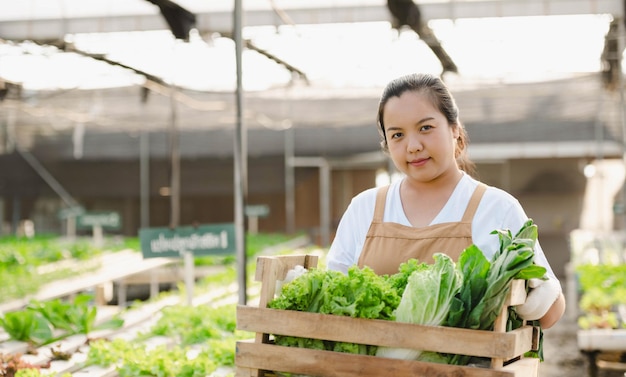 Portret van een Aziatische boerenvrouw met een houten kist vol verse rauwe groenten. Biologisch boerderijconcept.