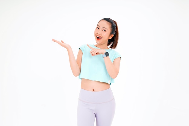 Portret van een Aziatische jonge, mooie en vrolijke vrouw in een sportoutfit met een vinger op kopieerruimte geïsoleerd op de achtergrond