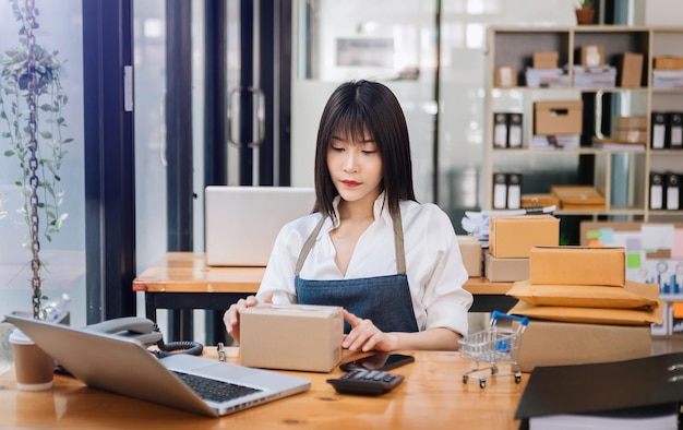 Portret van een Aziatische jonge vrouw mkb die werkt met een smartphone of tablet die online aankooporders ontvangt en controleert naar freelance bedrijf online en leveringsconceptxA