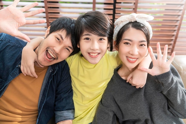 Portret van een Aziatische lieve familie die zit en glimlacht in de woonkamer, zoon knuffelt zijn ouder met liefdeshand, houdt vader en moeder arm van achteren vast en kijkt naar de camera met geluk en vrolijk thuis