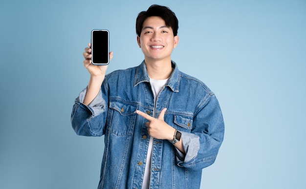 Portret van een Aziatische man die een jas draagt en een telefoon gebruikt op een blauwe achtergrond