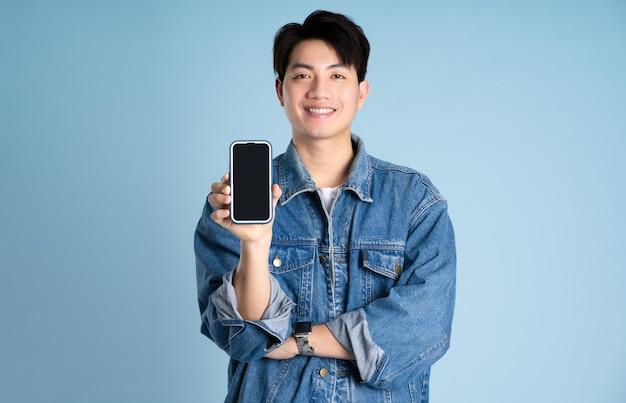 Portret van een Aziatische man die een jas draagt en een telefoon gebruikt op een blauwe achtergrond