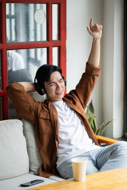 Portret van een Aziatische man die in een café zit met een telefoon en naar muziek luistert
