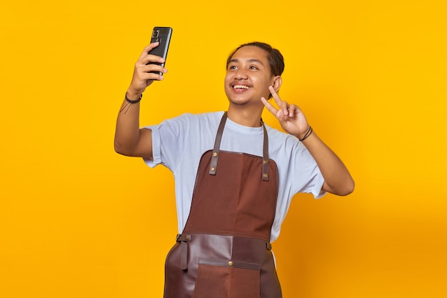 Portret van een aziatische man die lacht en een vredesteken toont terwijl hij een selfie op zijn mobiele telefoon neemt