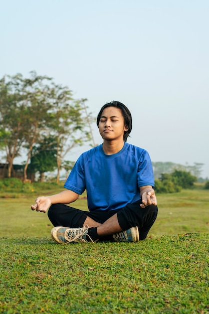 Foto portret van een aziatische man die meditatie doet in een groot groen veld green