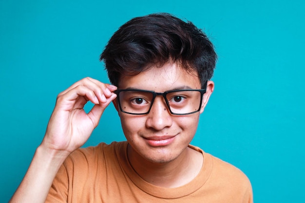 Foto portret van een aziatische man die naar de camera kijkt terwijl hij zijn bril vasthoudt op een blauwe achtergrond