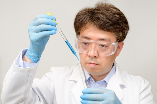 Foto portret van een aziatische mannelijke wetenschapper van middelbare leeftijd die een witte laboratoriumjas en handschoenen draagt en een experimentele container in zijn hand houdt.