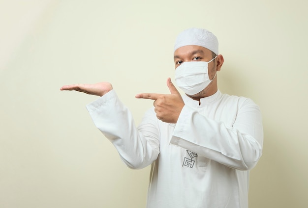 portret van een aziatische moslimman die een masker draagt en wijst naar iets aan zijn zijde te presenteren