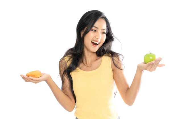 Portret van een Aziatische vrouw die een groene appel en een doughnut in beide handen houdt