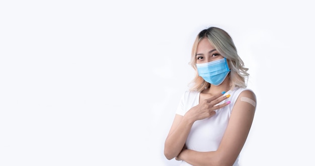 Portret van een Aziatische vrouw die een masker draagt en drie vingers vasthoudt voor de derde dosis vaccin op een witte achtergrond met kopieerruimte