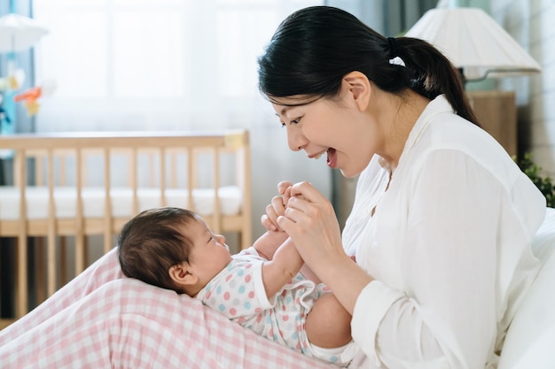 Portret van een aziatische vrouw vol vreugde als nieuwe moeder. vrolijke koreaanse mummie die de hand van haar baby zachtjes vasthoudt en kinderliedjes zingt. moederdag concept