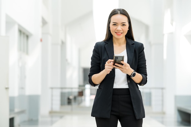 Portret van een aziatische werkende vrouw die een zwart pak draagt en een mobiele telefoon vasthoudt